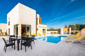 A modern building with a pool area, including a dining table with chairs and lounge chairs around the pool. - Villa Lidia Oura Beach with private Swimmingpool (Albufeira)