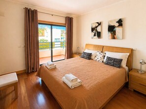 Habitación de hotel con una cama grande, cabecero de madera, mesita de noche, lámpara de noche y vistas al exterior.