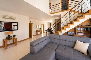Una sala de estar moderna con un sofá seccional gris, una escalera de madera y una estantería llena de libros.