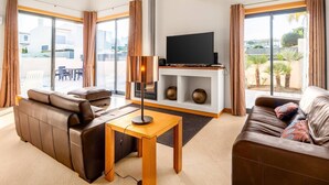 A modern living room with leather sofas, a wooden coffee table, and a flat-screen TV on a white shelf.
