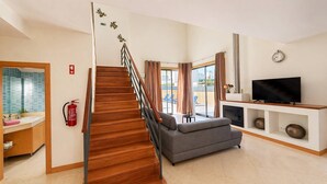 A modern living room with a wooden staircase, a grey sofa, a flat-screen TV, and a fireplace.