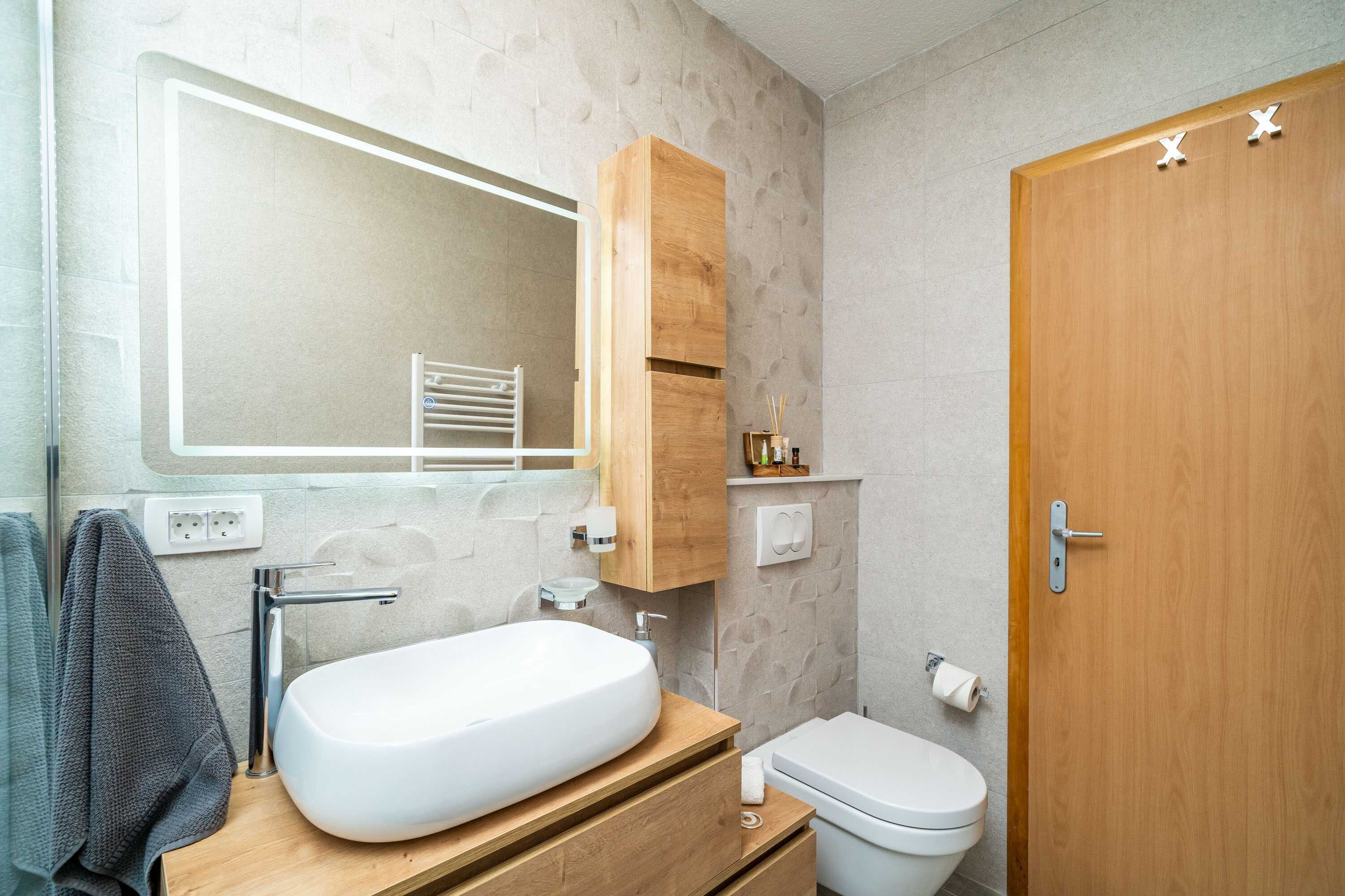 Ein modernes Badezimmer mit einem weißen Waschbecken, einer Holz-Kommode und einer Toilette.