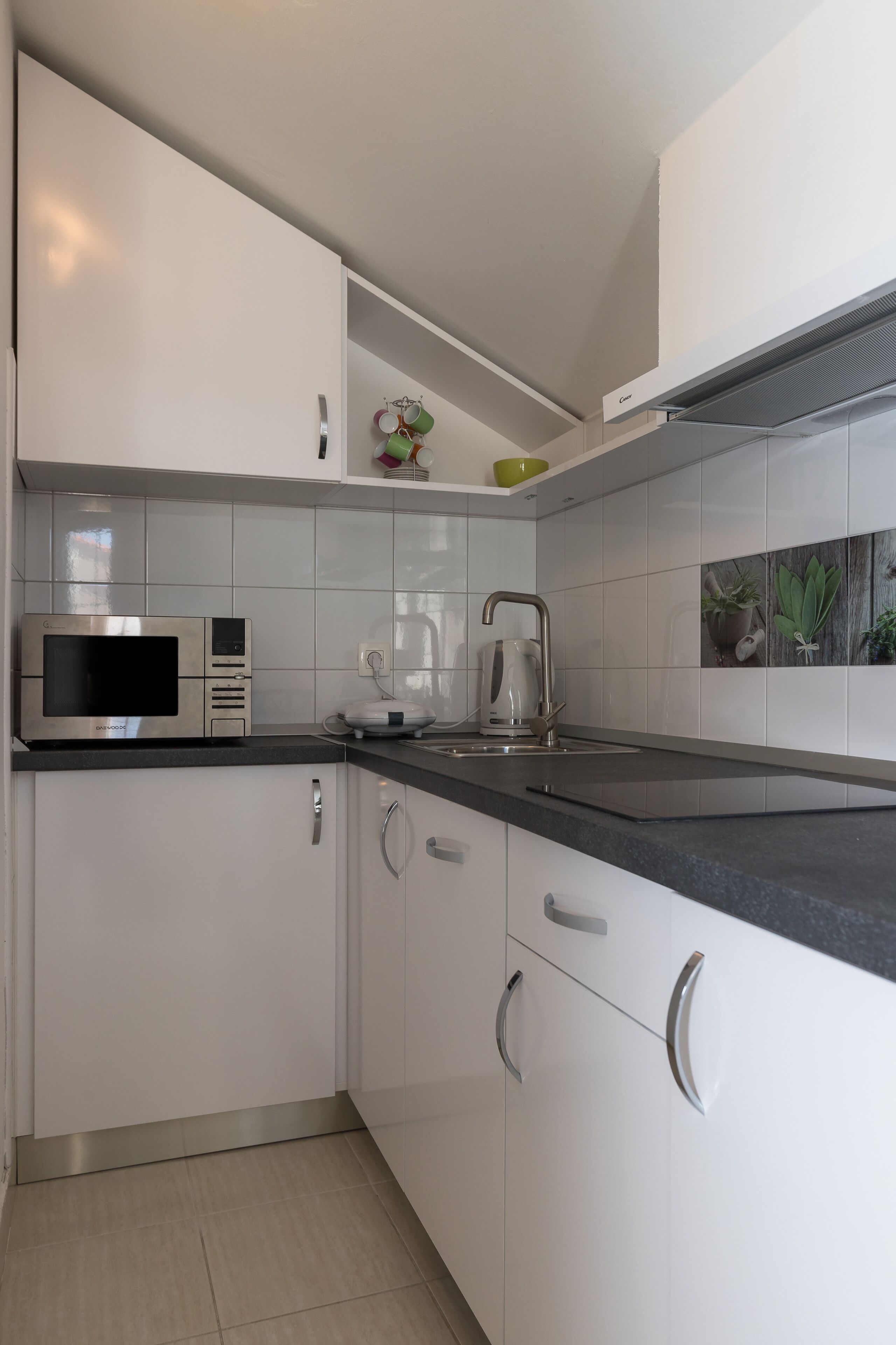 A modern kitchen with white cabinets, a stainless steel microwave, a kettle, and a black countertop.