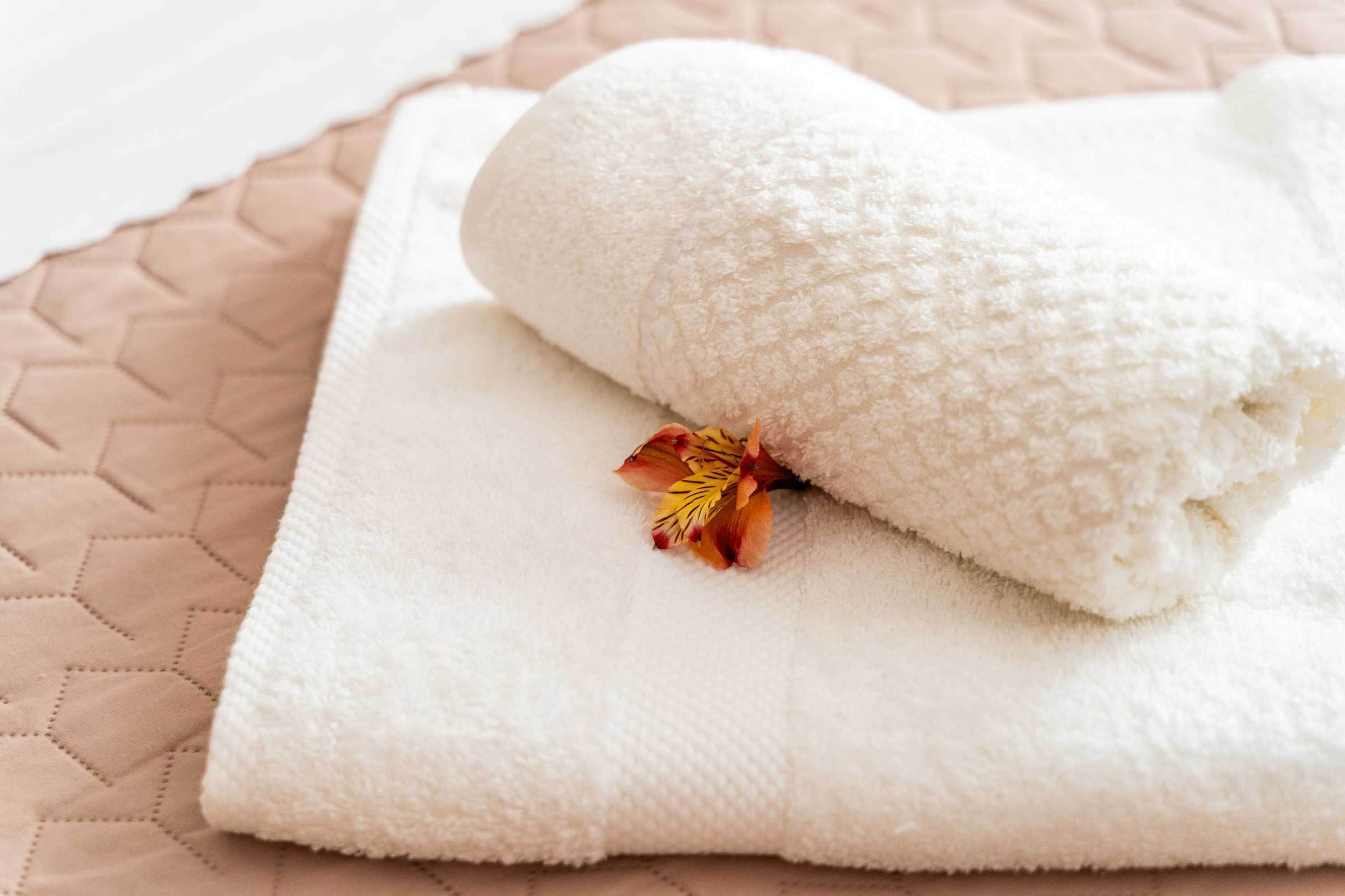 Una toalla blanca doblada con un detalle floral seco sobre una superficie beige acolchada.