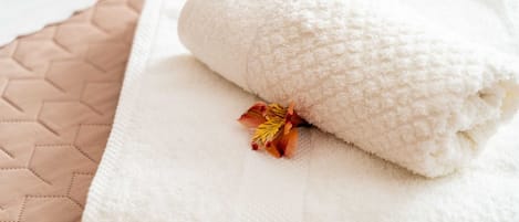 A neatly folded white towel with a dried flower on a beige quilted surface.