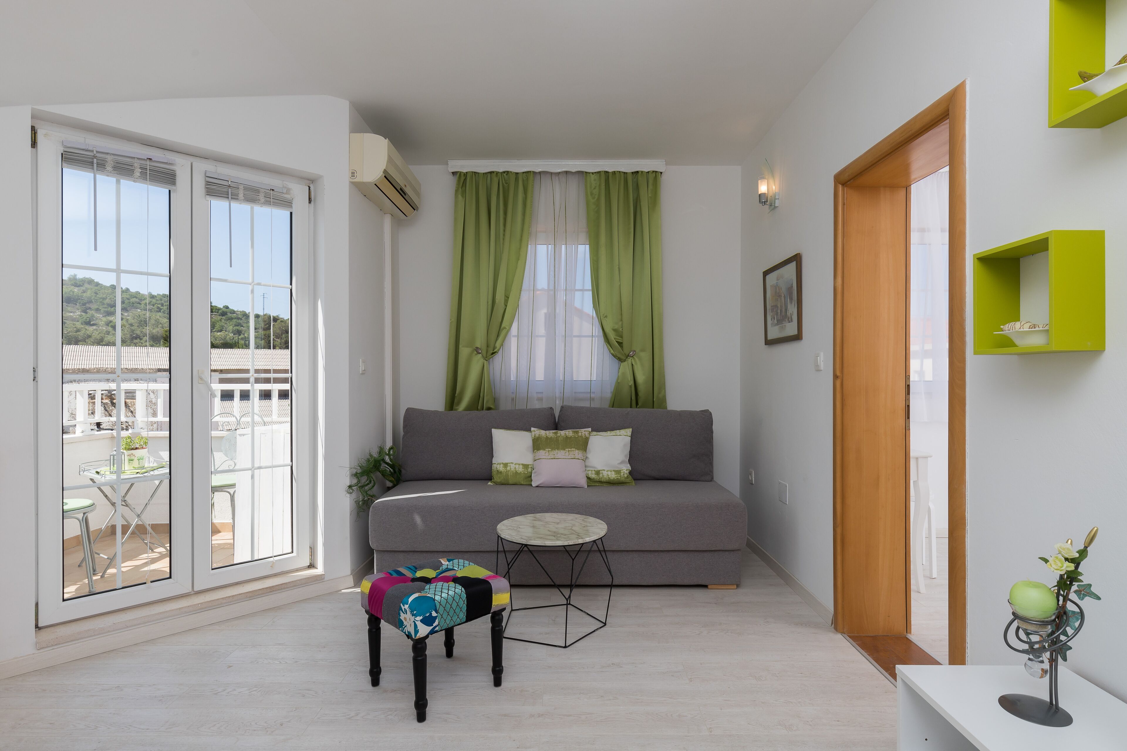 Ein modernes Wohnzimmer mit einem grauen Sofa, einem kleinen runden Tisch und einem farbenfrohen Hocker.