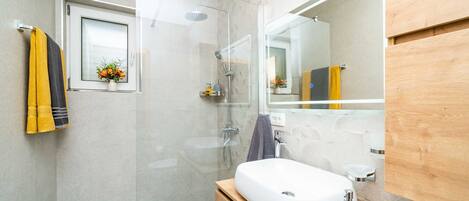 Un baño moderno con cabina de ducha de vidrio, tocador de madera y un espejo grande.