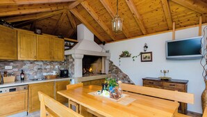 Uma cozinha rústica com armários de madeira, parede de pedra, lareira e mesa de jantar de madeira com bancos.