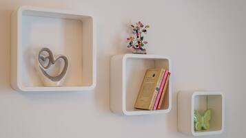 Tres repisas blancas montadas en la pared con un objeto con forma de corazón, un pequeño árbol decorativo y libros.