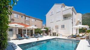 Piscina com espreguiçadeiras e guarda-sóis, cercada por edifícios com varandas e um céu azul límpido.