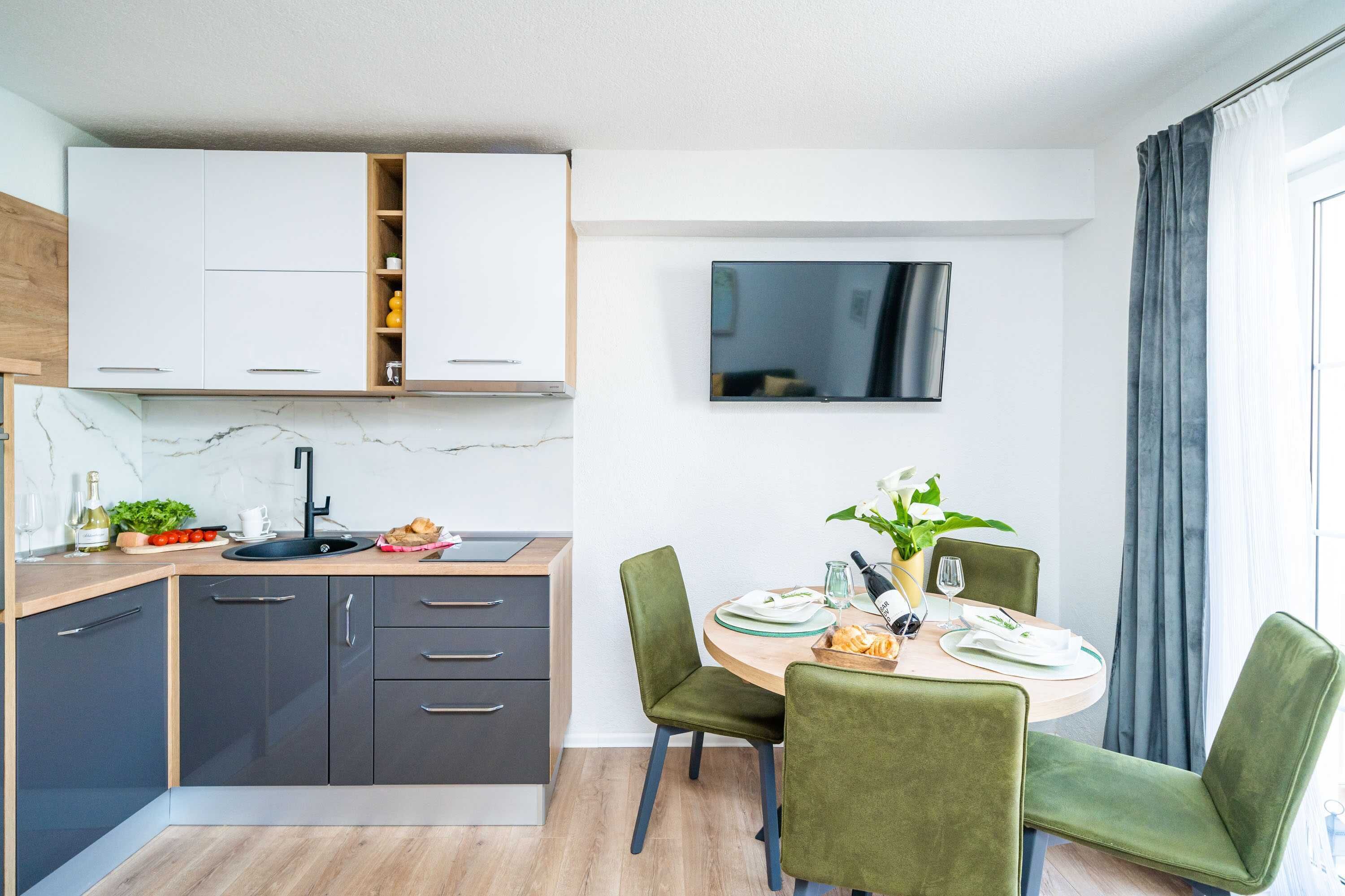 Una cocina moderna con armarios grises oscuros, encimera de mármol y un comedor con sillas tapizadas en color verde.