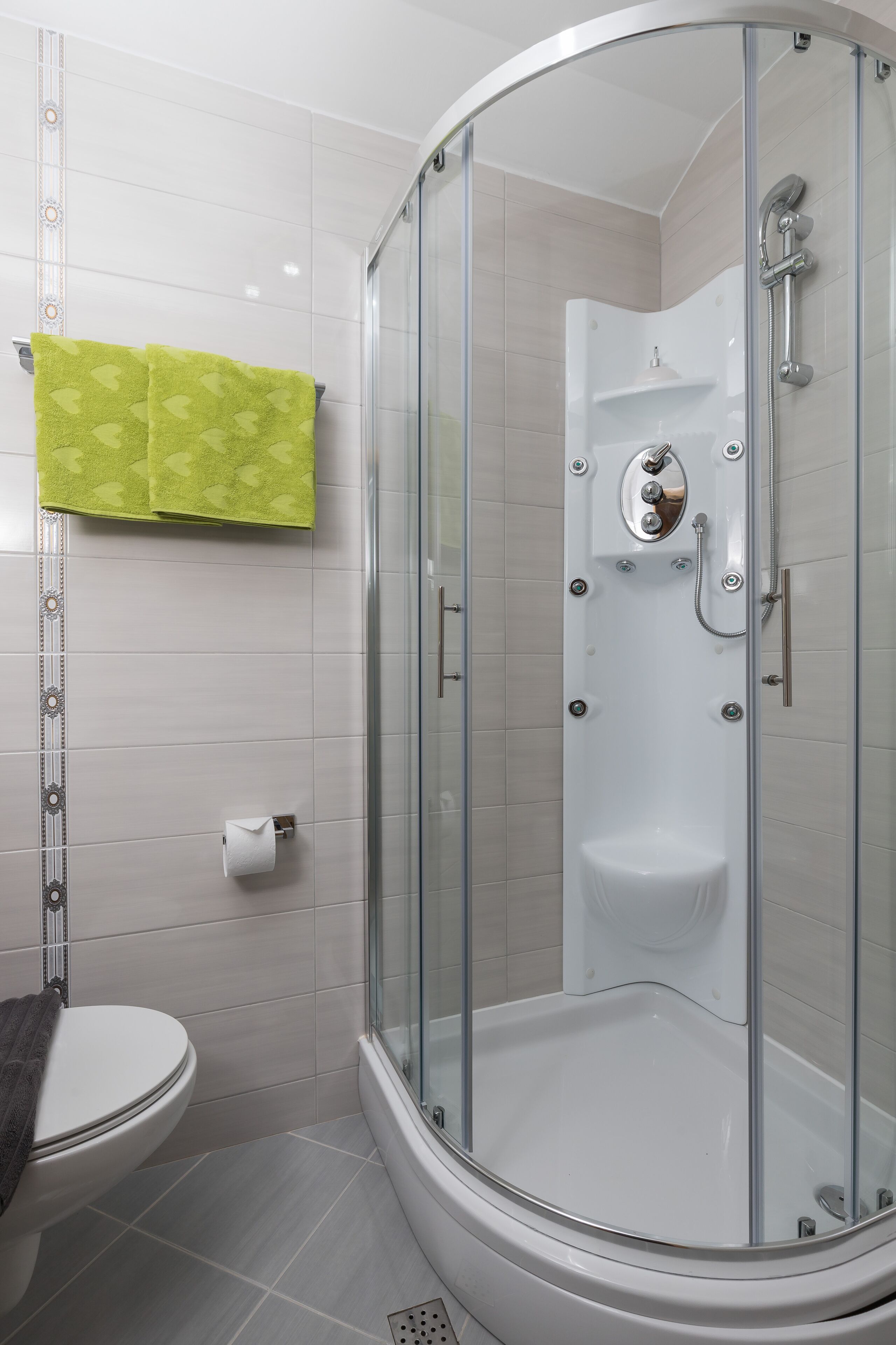 A modern bathroom with a glass-enclosed shower, a toilet, and a towel rack with a green towel.