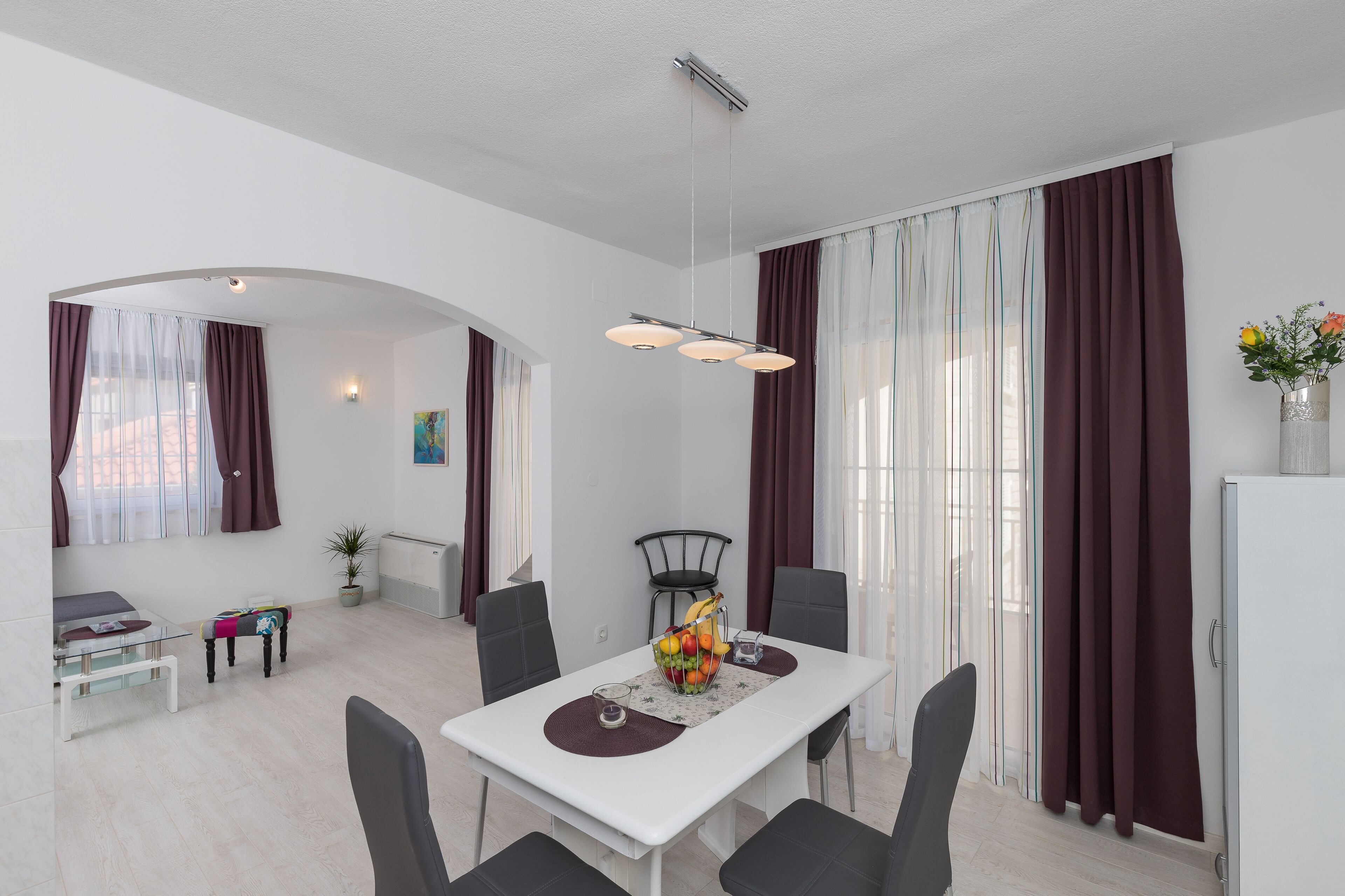 A modern dining area with a white table, black chairs, and a fruit bowl centerpiece.
