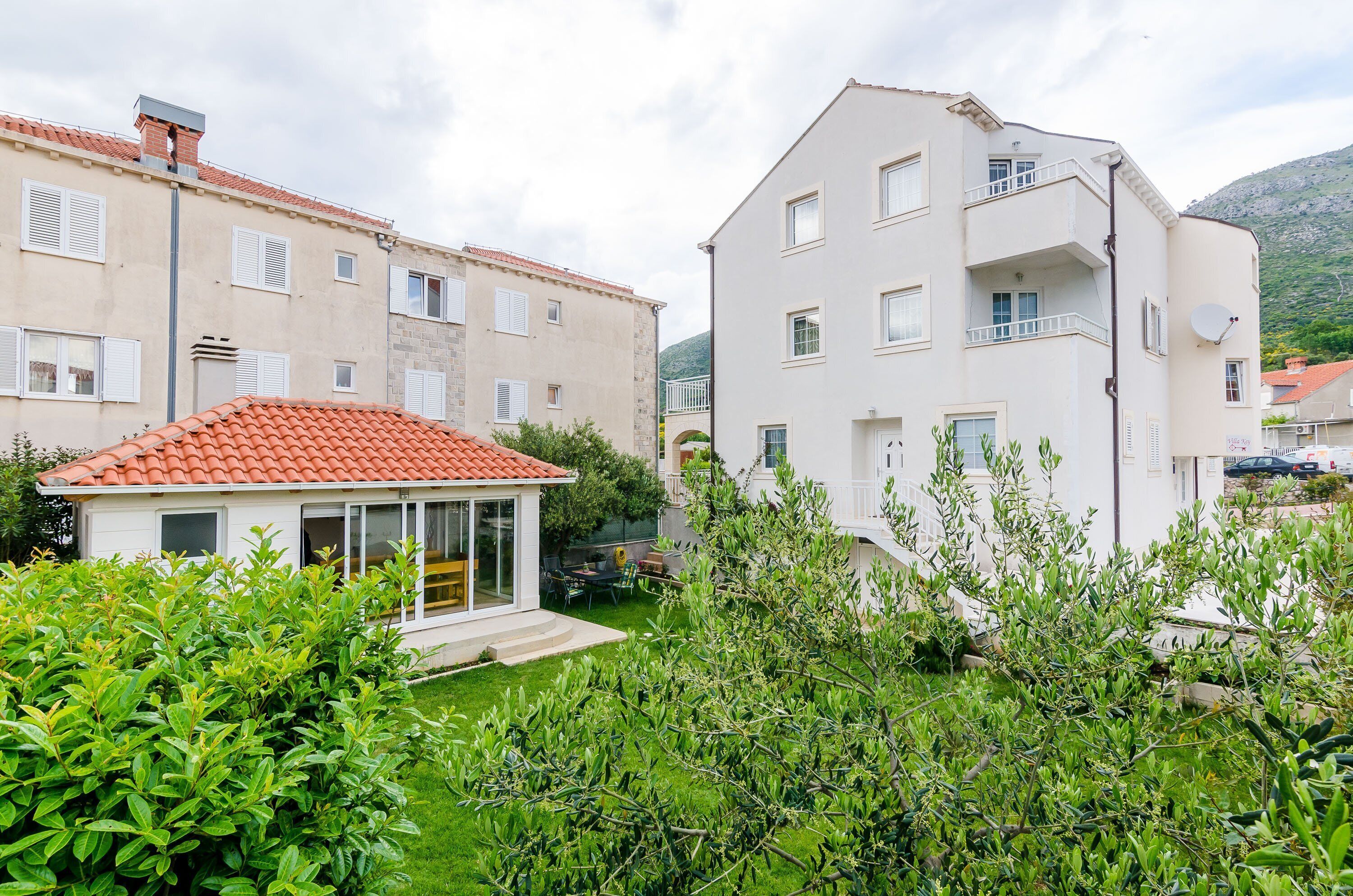 A residential building with a red-tiled roof, white exterior walls, and a balcony.