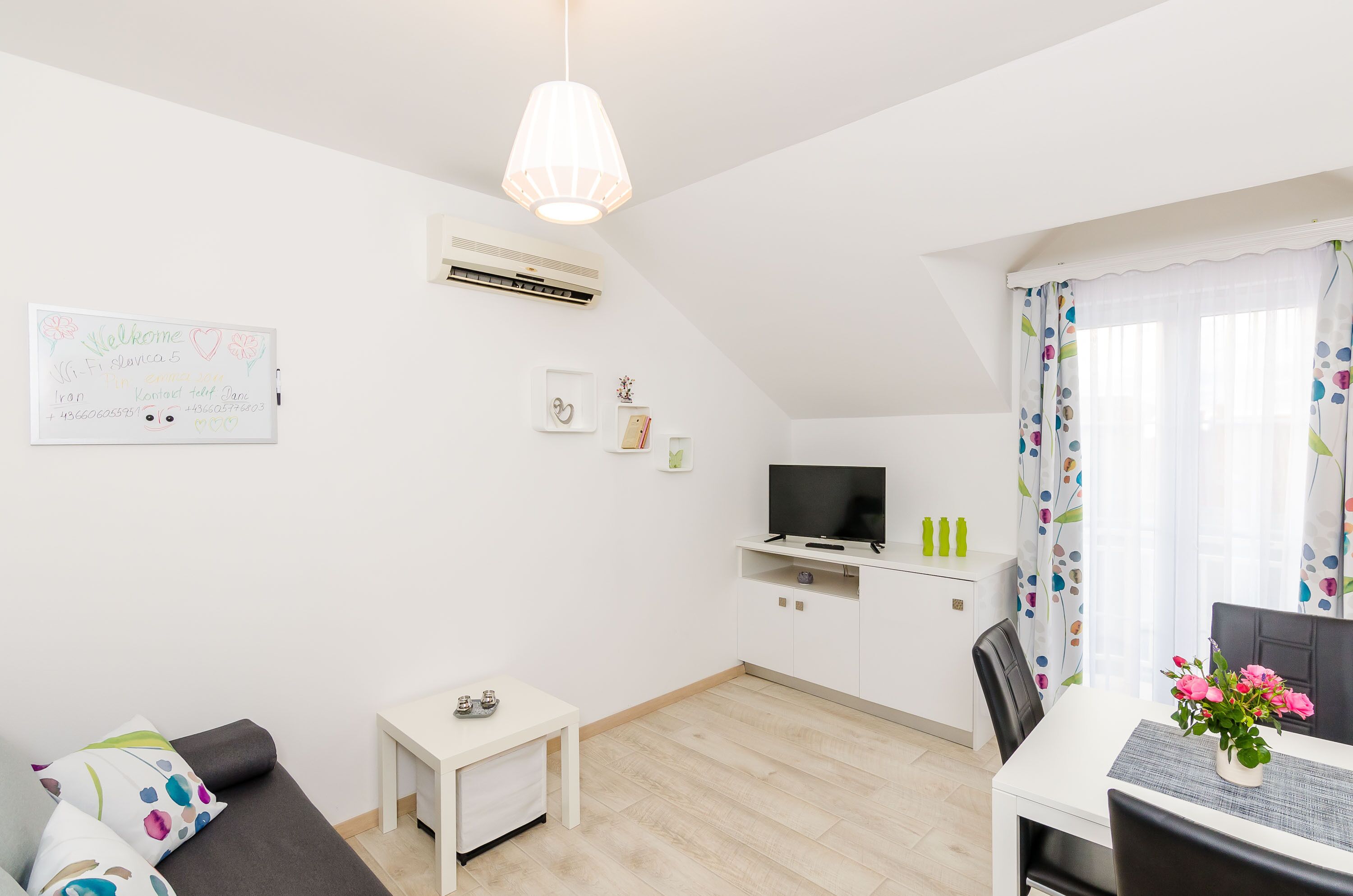 Una sala de estar moderna y bien iluminada con una televisión de pantalla plana, una pequeña mesa blanca, un sofá y una lámpara en el techo.