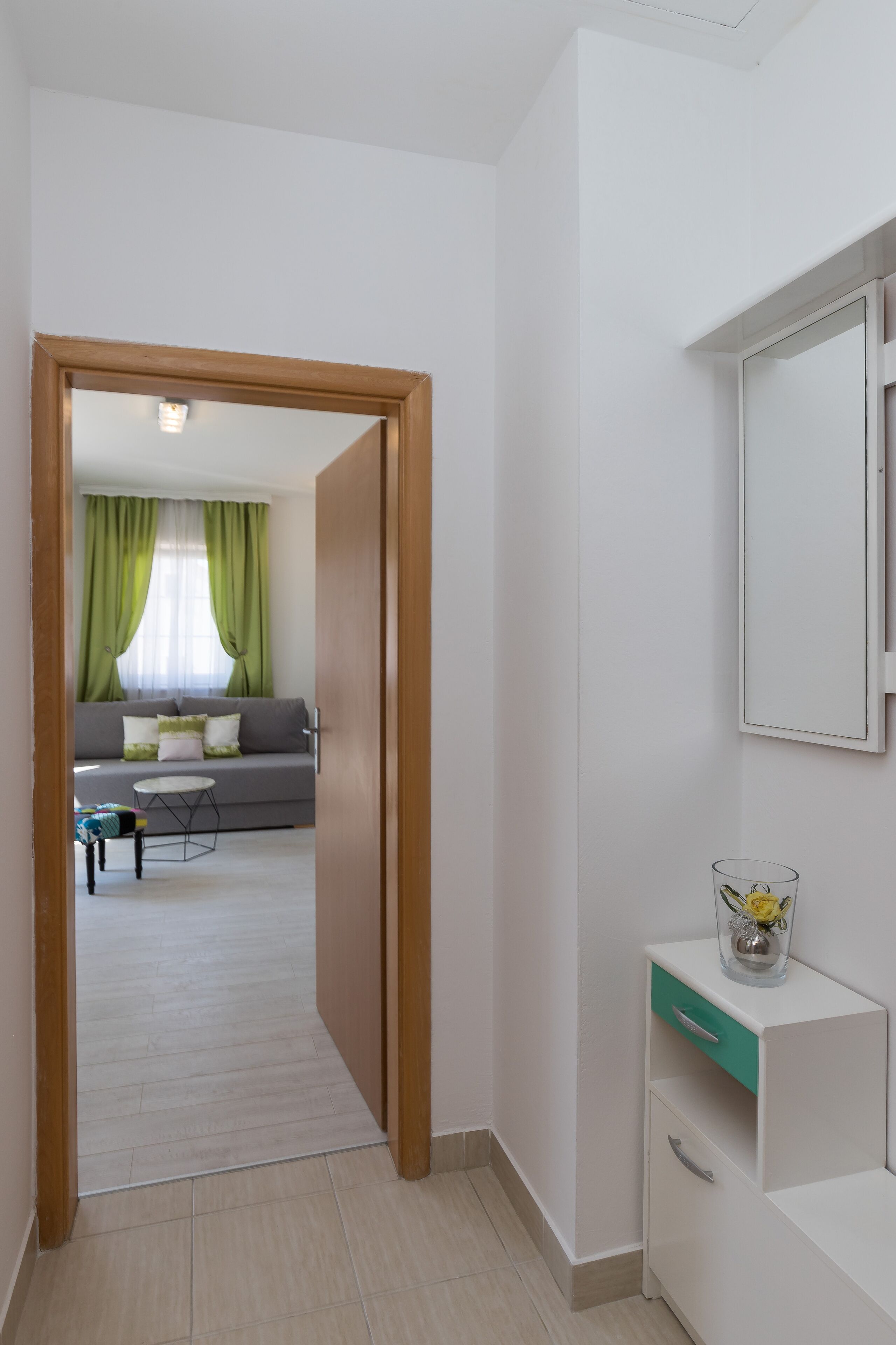 A hallway leading to a living area with a sofa, a small table, and a cabinet with a mirror.