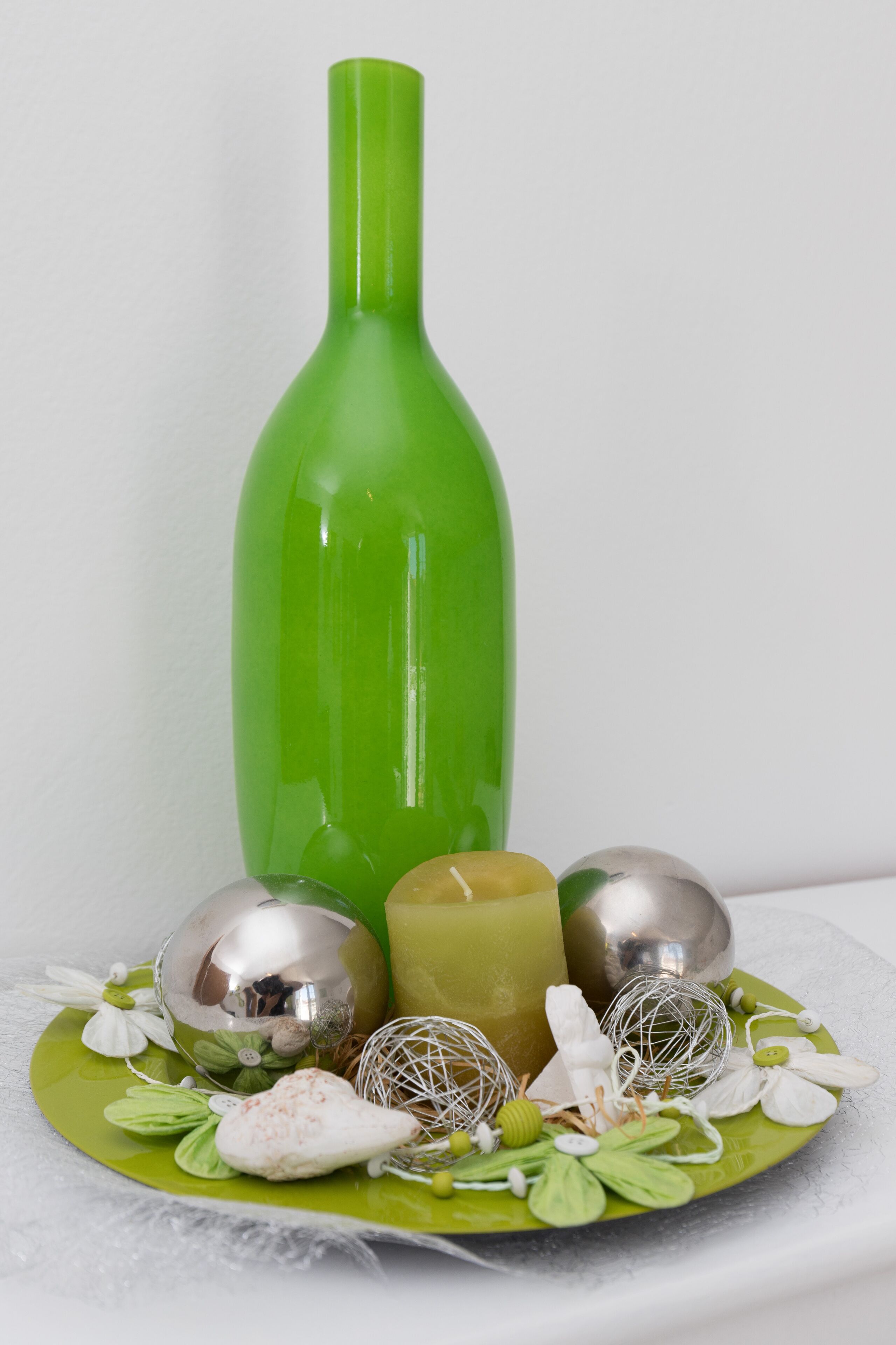Un jarrón verde, una vela y adornos sobre un plato.