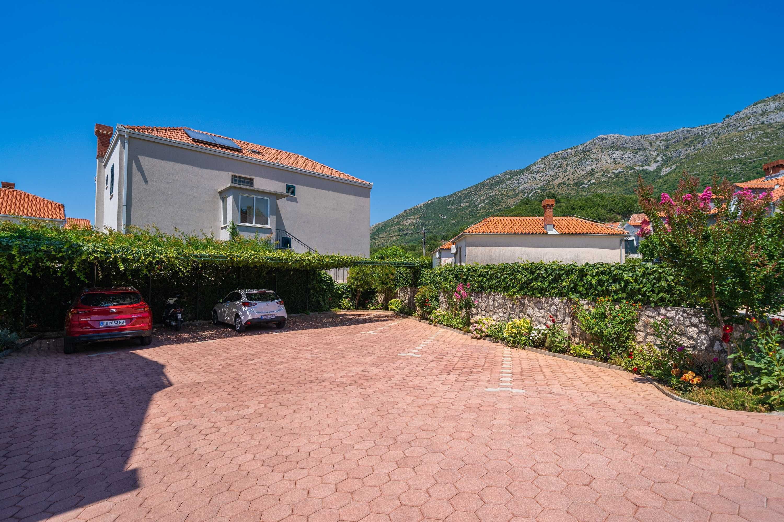 A paved driveway leading to a house with a red car parked on the left.