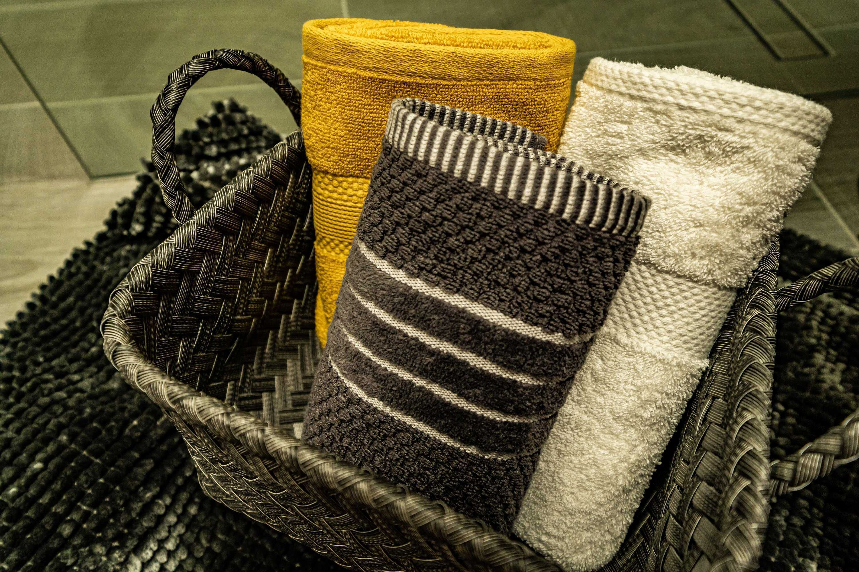 Un panier tressé contenant trois serviettes aux motifs différents.
