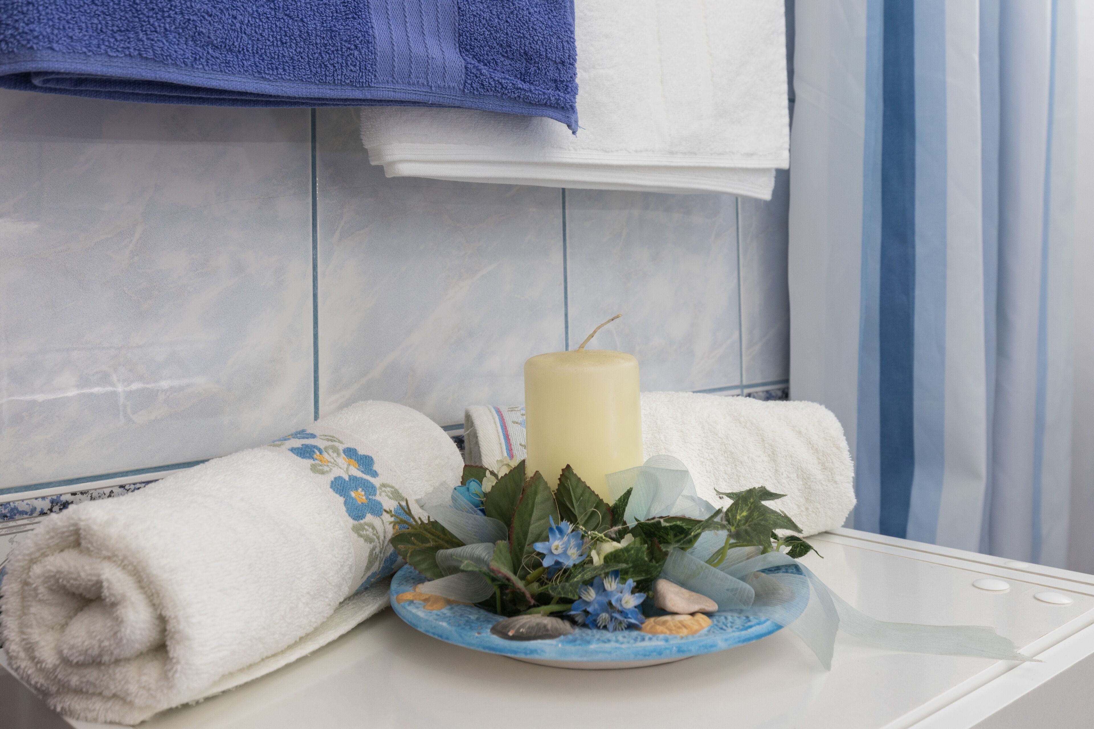 Ein Badezimmer mit einer weißen Badewanne, einem blauen Handtuch und einer dekorativen Anordnung mit Kerze und Blumen.
