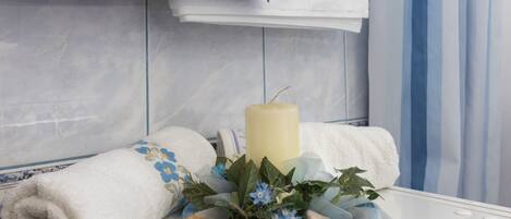 A bathroom with a white bathtub, a blue towel, and a decorative arrangement with a candle and flowers.