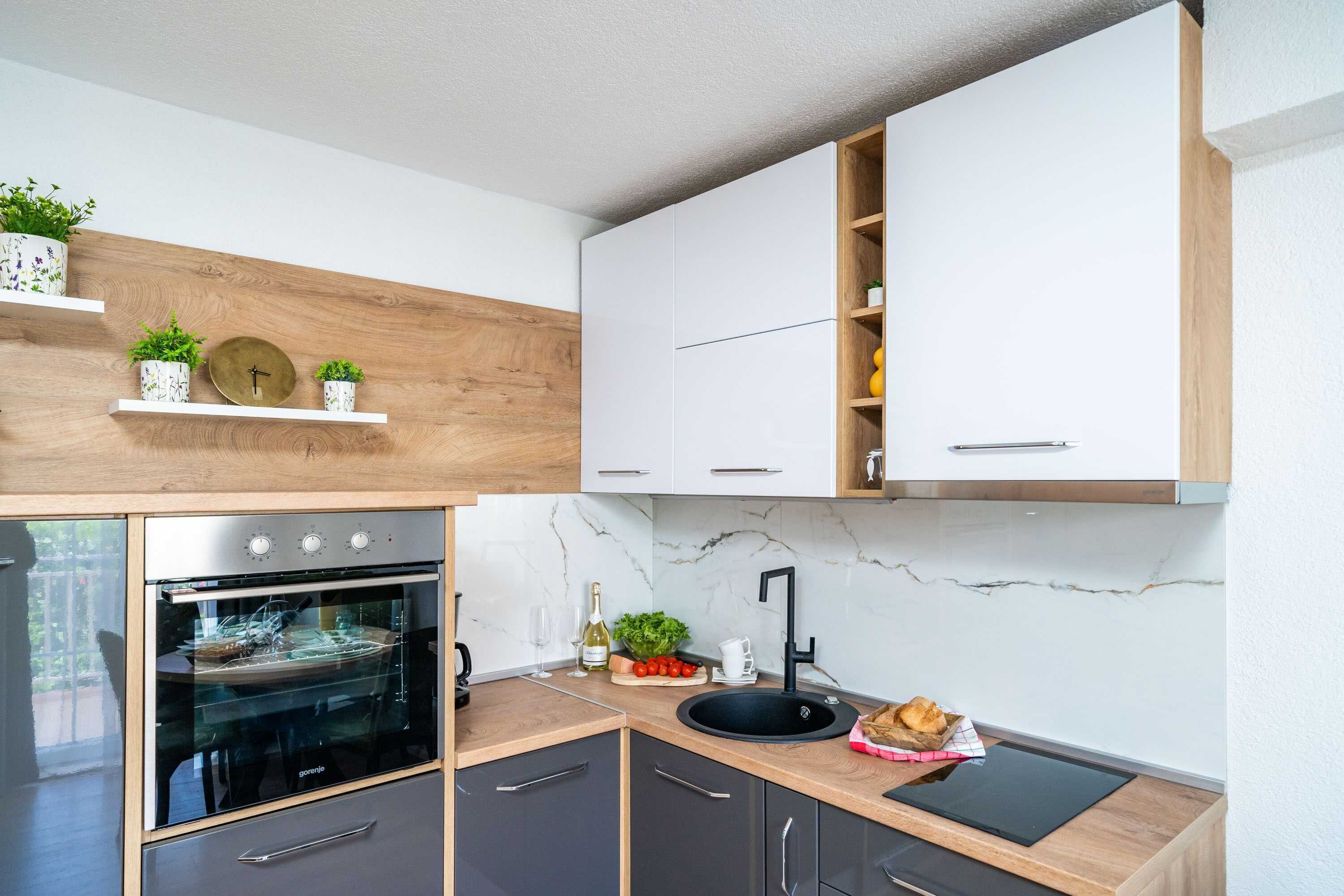 Una cocina moderna con horno empotrado, salpicadero de mármol y estanterías de madera con plantas.