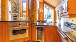 A kitchen with wooden cabinets, a stone wall, a built-in oven, a microwave, and a large window.