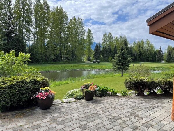 Um pátio com plantas em vasos, um lago e um campo de golfe ao fundo.