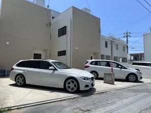 Une BMW blanche, modèle break, était garée devant un immeuble de couleur beige, avec un trottoir en béton.