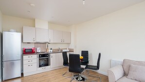A compact kitchen with a microwave, oven, and refrigerator. There is a dining table with chairs and a sofa in the living area. - Golden Heights 9 (Maidstone)