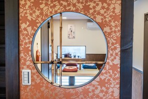 Un miroir rond reflète une pièce dont le mur est orné d’un motif, et où l’on aperçoit un ordinateur et un canapé.