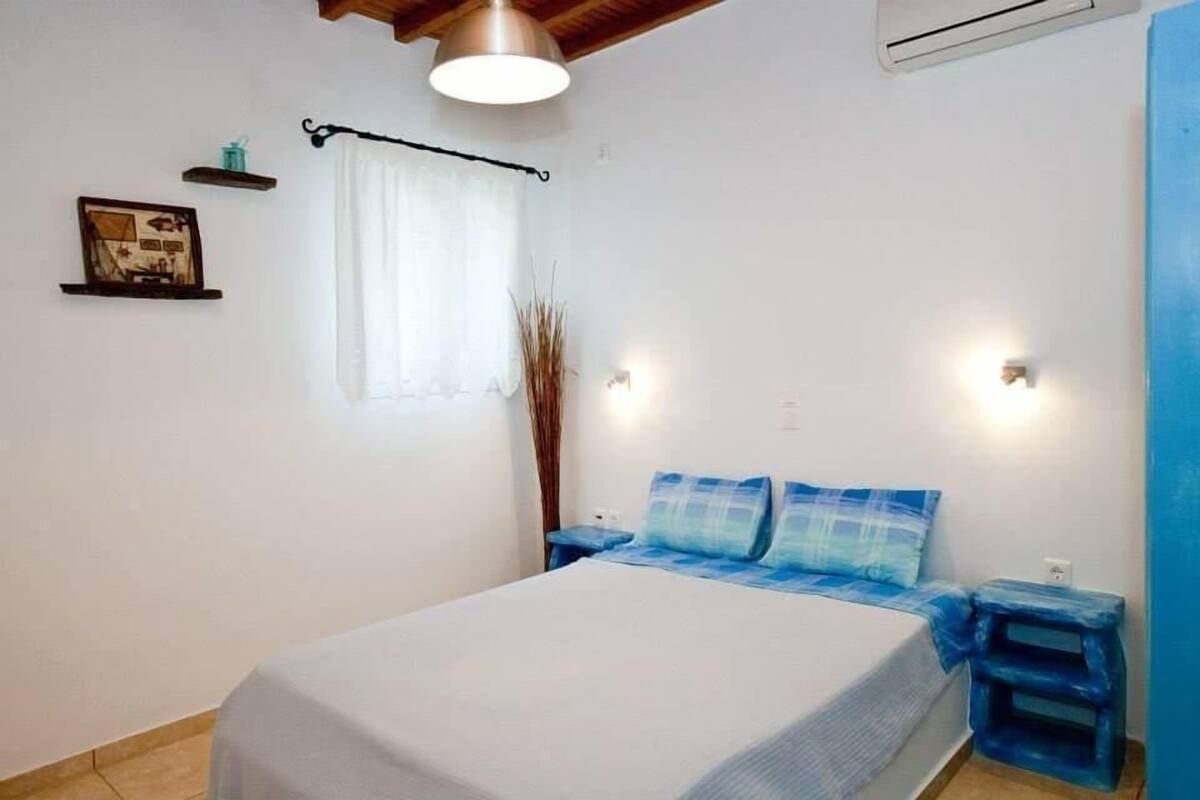 Un dormitorio con cama, mesitas de noche, una ventana con cortinas, luces fijadas a la pared y un ventilador de techo.