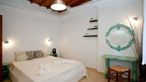 Un dormitorio con cama, mesitas de noche, un tocador, un espejo y un taburete pequeño.