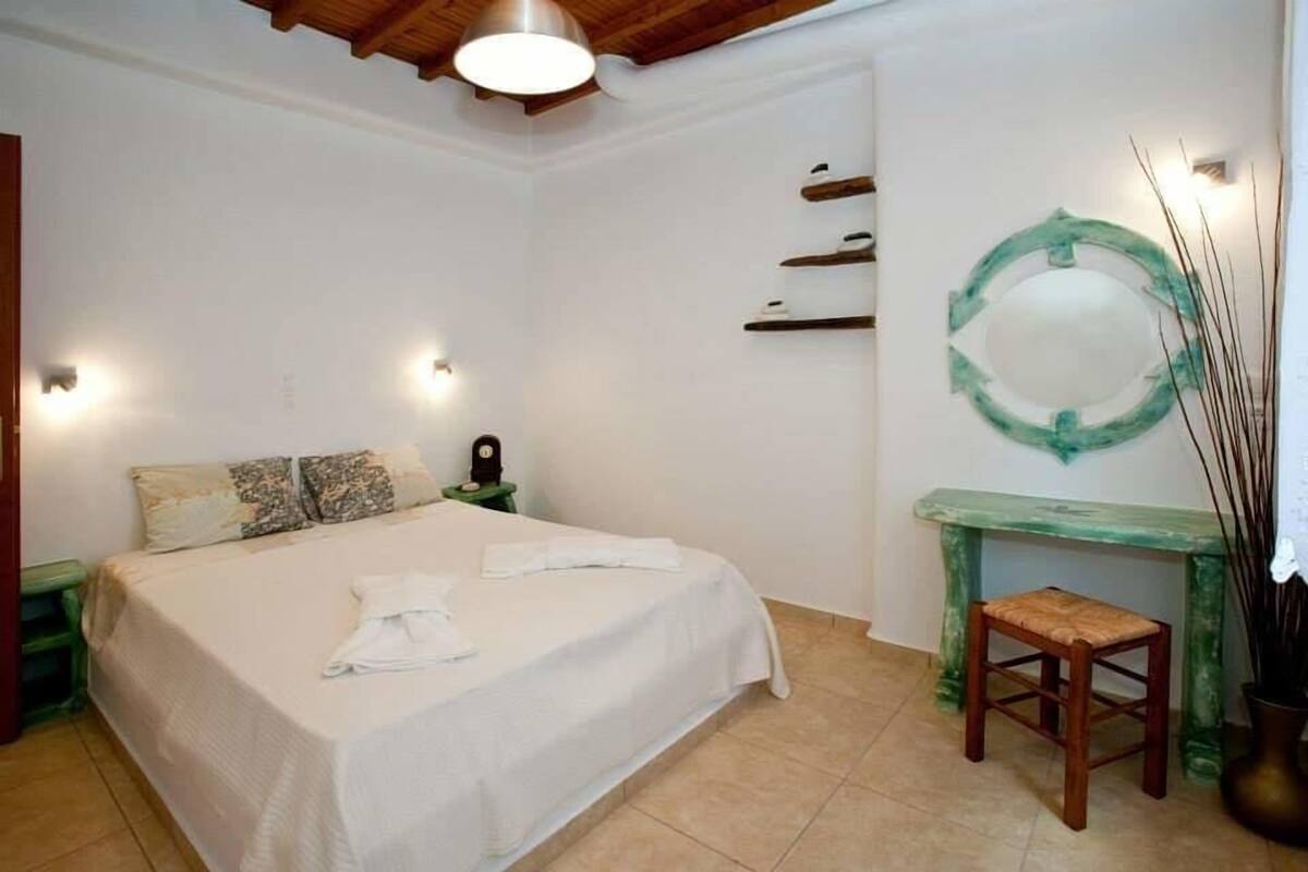 Un dormitorio con cama, mesitas de noche, un tocador, un espejo y un taburete pequeño.