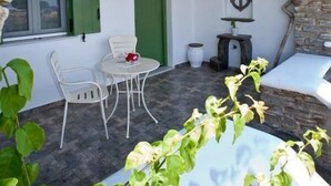 Un arco de piedra que da a un patio con una mesa y sillas, una puerta verde y un adorno de ancla en la pared.