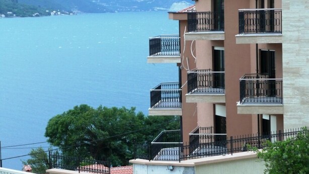 A multi-story building with balconies overlooking a body of water and mountains in the background.