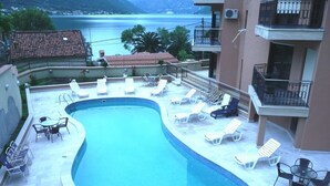 A swimming pool with lounge chairs and tables, surrounded by a building with balconies.