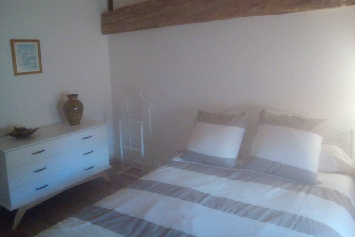 Une chambre à coucher avec un lit, une commode et un vase posé sur la commode.