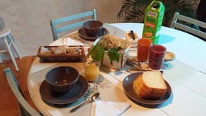 Ett matbord med en korg med bröd, en skål, ett glas juice, en flaska apelsinjuice och en tallrik med en smörgås.