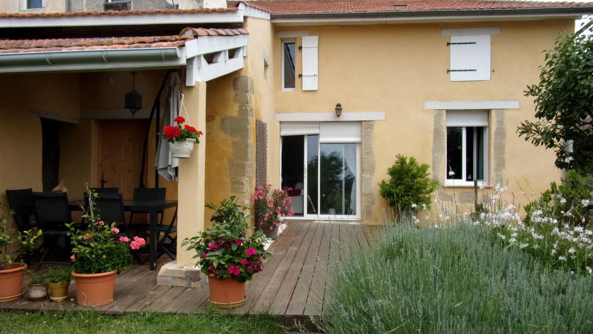 Une maison dotée d’un patio couvert, d’une terrasse en bois et de plantes en pot.