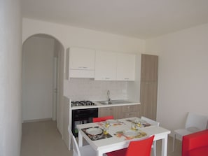 Une cuisine de taille réduite avec des meubles blancs, un évier et une table à manger entourée de chaises rouges.