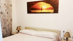 A bedroom with a bed, a nightstand, a lamp, a painting of a sunset, and a curtain. - Affittimoderni Castelsardo Incanto - Csso15 (Castelsardo)