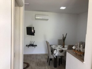 A dining area with a table, chairs, a flat-screen TV mounted on the wall, and a ship model on the counter. - Stanovic Bungalow  2 (Ulcinj)