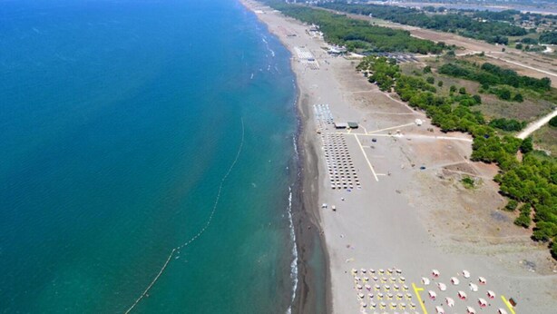 Vue aérienne d’une zone côtière comprenant une plage, des parkings et une route menant à une ville.