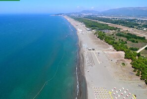 Vista aérea de uma área costeira com praia, estacionamentos e uma estrada que leva a uma cidade.