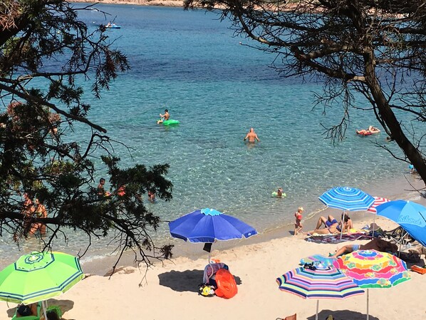 A beach with clear water, umbrellas, and people swimming.