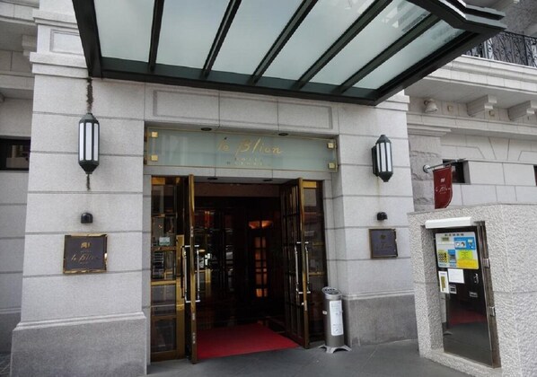 The entrance to a hotel with a glass canopy, a red carpet, and a sign above the doors.