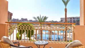 A balcony with wicker furniture, a pool, and palm trees. - Parrotel Lagoon Waterpark Resort (Sharm El Sheikh)