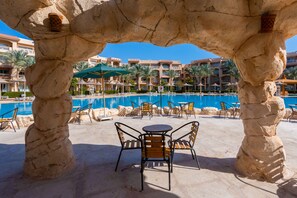 Un área de piscina con pilares de piedra, sillones de descanso y sombrillas.