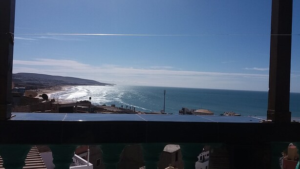 A view of a beach from a window overlooking a coastal area with buildings and a clear sky. - Bassi Apartment (Taghazout)